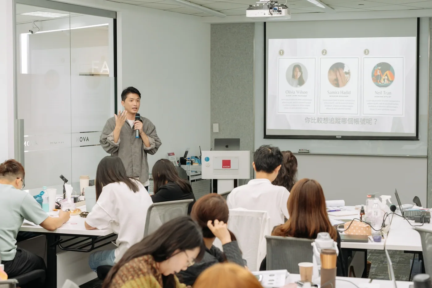 韓森在企業會議室裡拿著麥克風授課,學員圍著長桌做筆記
